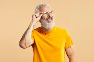 An older man with white hair and a beard wearing a yellow t-shirt and glasses
