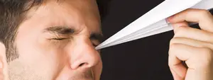 A man is blowing his nose with a tissue and closing his eyes