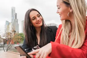 Two women smiling and talking while looking at a cell phone on a table