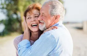 Old man and woman hugging at the beach with smiles on their faces