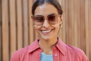 Woman wearing sunglasses smiling in front of a wooden wall