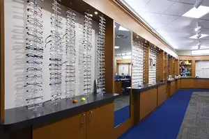 An optician's shop with a variety of eyeglasses on display and a blue carpet on the floor.