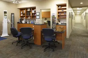 An indoor view of an office room with chairs, shelves, and mirrors in a room with ceiling lights and a carpeted floor.