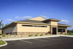 A commercial building with a parking lot and green field in the background