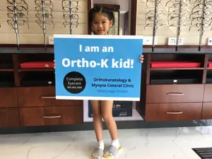 A girl is standing and holding a sign that says I am an Ortho-K kid