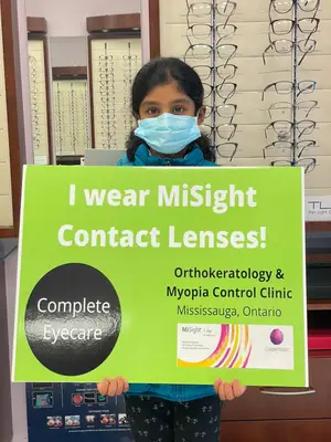 A girl holds a sign that reads 'I wear MiSight Contact Lenses' inside an optometrist's office.