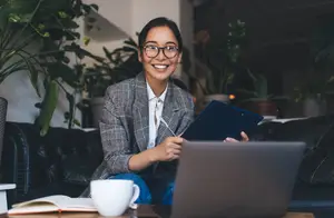A woman sitting on a couch smiling and holding a pen and folder.