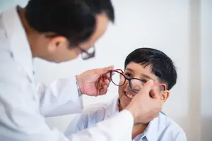A doctor is adjusting a boy's glasses in a medical setting