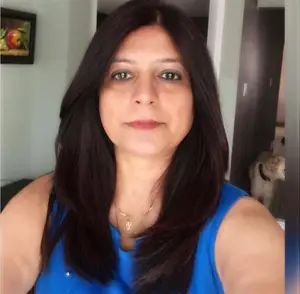 Woman with long black hair and blue sleeveless top standing inside a room