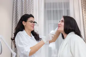 A woman is getting a dental checkup by a dentist wearing a white coat and gloves in a dental clinic.