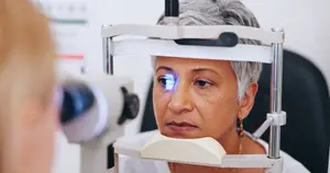 An older woman with gray hair is having her eyes examined by a doctor in a clinic.