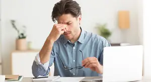 A man sitting at a desk with his hand on his forehead, looking stressed.