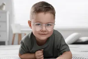 A smiling young boy with glasses lying on a bed with pillows in a room