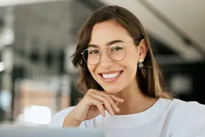 A smiling woman with glasses and earrings sitting in an office.