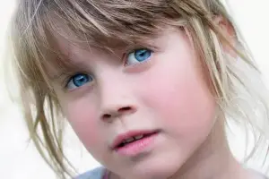 Close-up of a young girl with blue eyes and blonde hair looking directly at the camera