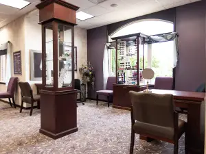 Interior of an office with a desk and chairs, a flower vase, and a glass display cabinet, all in purple color scheme.