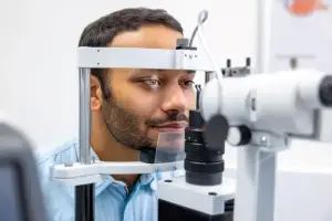 A man is looking through a microscope while wearing a blue shirt