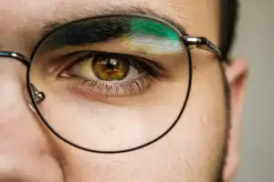 A close up of a man's eye with green and yellow paint on his eyebrow and eyelashes