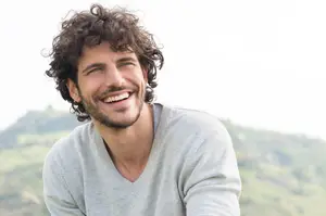 A man with curly hair and a beard is smiling and posing for a photo.