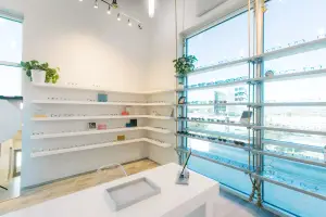 An empty boutique with white shelves, a desk, and large windows, showcasing various glasses on display.