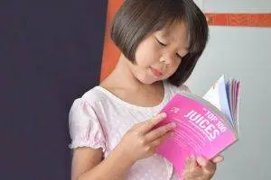 A young girl with short hair is reading a book titled Top 10 Juices