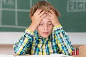 A boy sitting in a classroom with his head in his hands, appearing stressed.