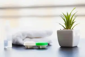 A white table with a bottle of water, a white towel, a small green plant, and a green and white colored container with a lid on it.