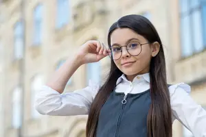 A girl with long hair and glasses standing in front of a building