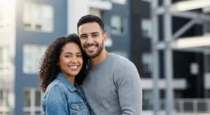 A man and woman smiling at the camera outside of an apartment building.
