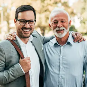 Two men standing in an outdoor area, one with a beard, smiling and posing for a photograph