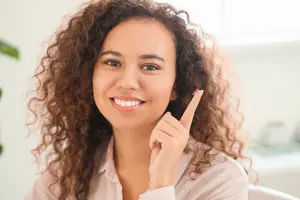 Woman with curly hair smiling and pointing her finger while wearing a pink shirt.