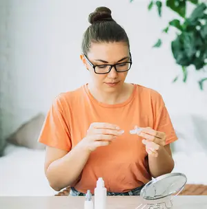 young woman putting on contact lenses orange shirt