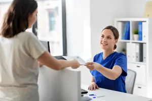 Two women in a medical office one is smiling and handing a paper to the other
