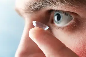 Close up of a man wearing a contact lens on his right eye while holding a contact lens on his left hand