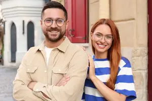 A man and woman smiling and standing with arms crossed in front of a building