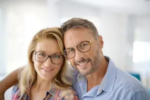 An older man and woman wearing glasses are posing for a picture while smiling