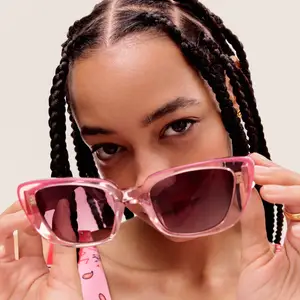 Close-up of a woman holding pink sunglasses with reflection of hand and glasses