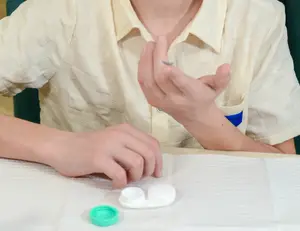 A boy in a yellow shirt is about to insert a contact lens into his eye.