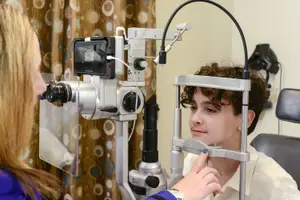 A woman is using an ophthalmoscope to examine a young man's eyes.