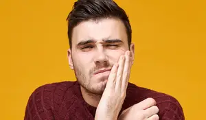 A man in a maroon sweater with his hand on his face