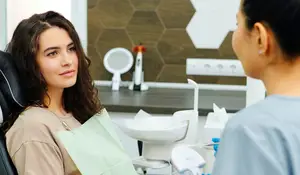 A woman is sitting in a dental chair and talking to a dental hygienist.