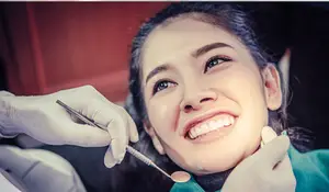 A woman sitting in a dental chair with a dentist cleaning her teeth.