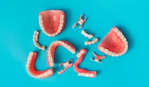 A collection of pink and white artificial teeth and dental components are arranged on a blue background.