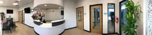 A white and wood colored medical reception area with a receptionist desk, doors, and potted plants.