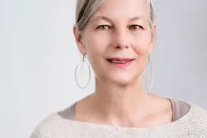 Close-up of a woman with gray hair, wearing earrings, smiling, and looking at the camera