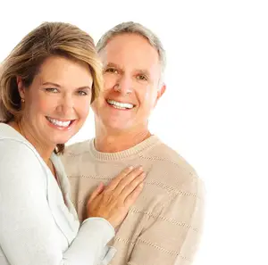 A smiling adult couple standing close to each other with the woman's hand on the man's chest.