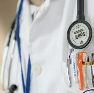 A doctor wearing a white coat with a stethoscope and various tools in their pocket.