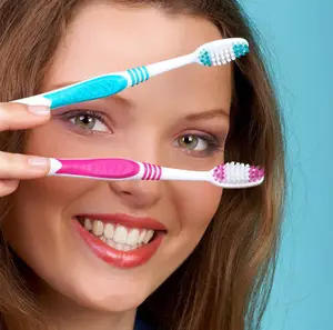 A woman holding two toothbrushes, one with pink and white bristles and the other with blue and white bristles, is smiling and looking at the camera.