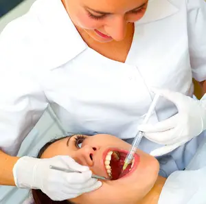 A dentist in white gloves and a mask is performing a dental procedure on a patient in a dental clinic.