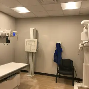 A room with a medical X-ray machine, a chair, and a blue jacket hanging on the wall.